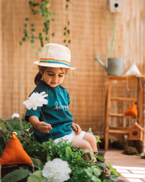 یک کودک در فضای باز آتلیه کودک نشسته و در حال باز با فضای سر سبز و گیاهان است